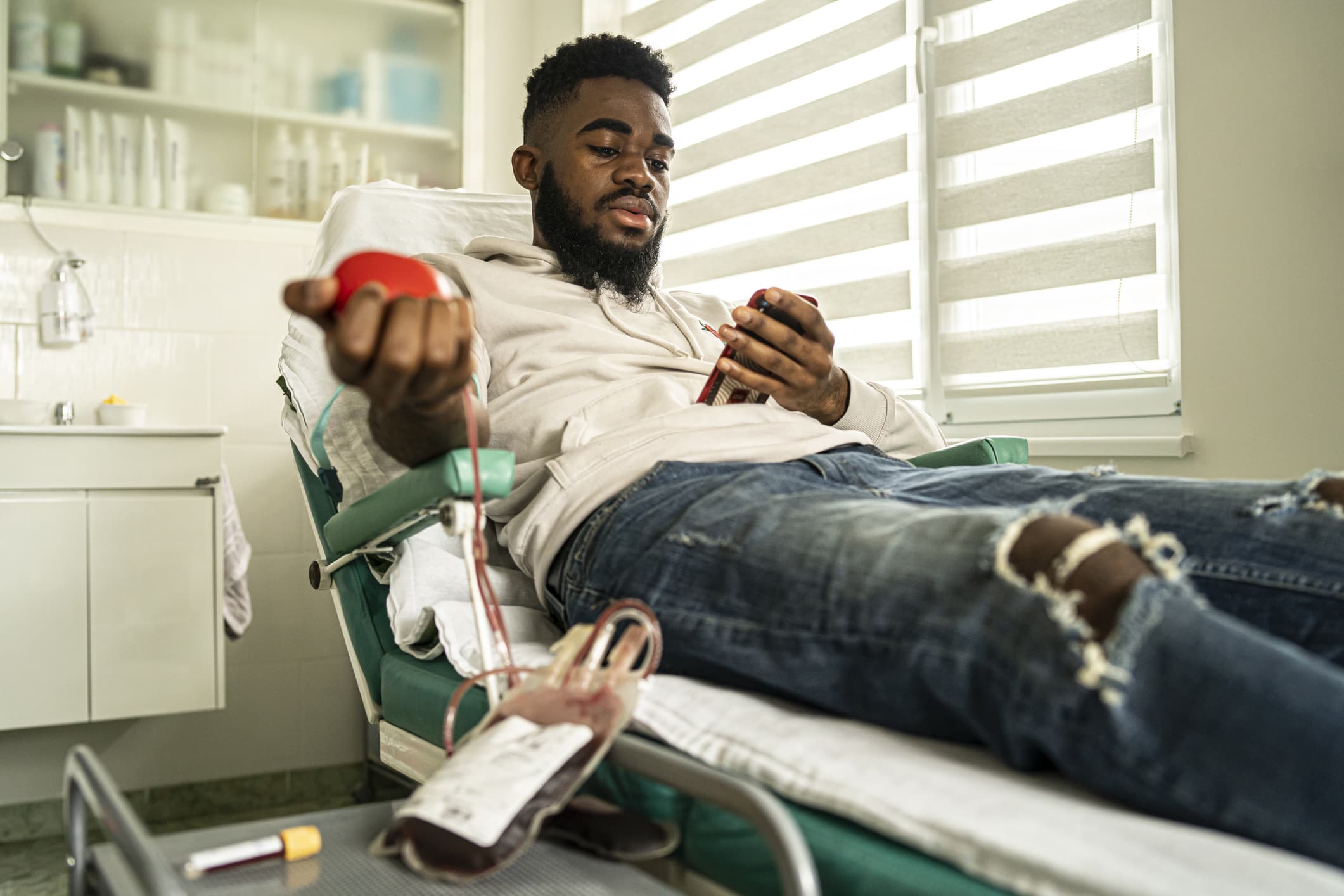 A young man donating blood and using his phone.