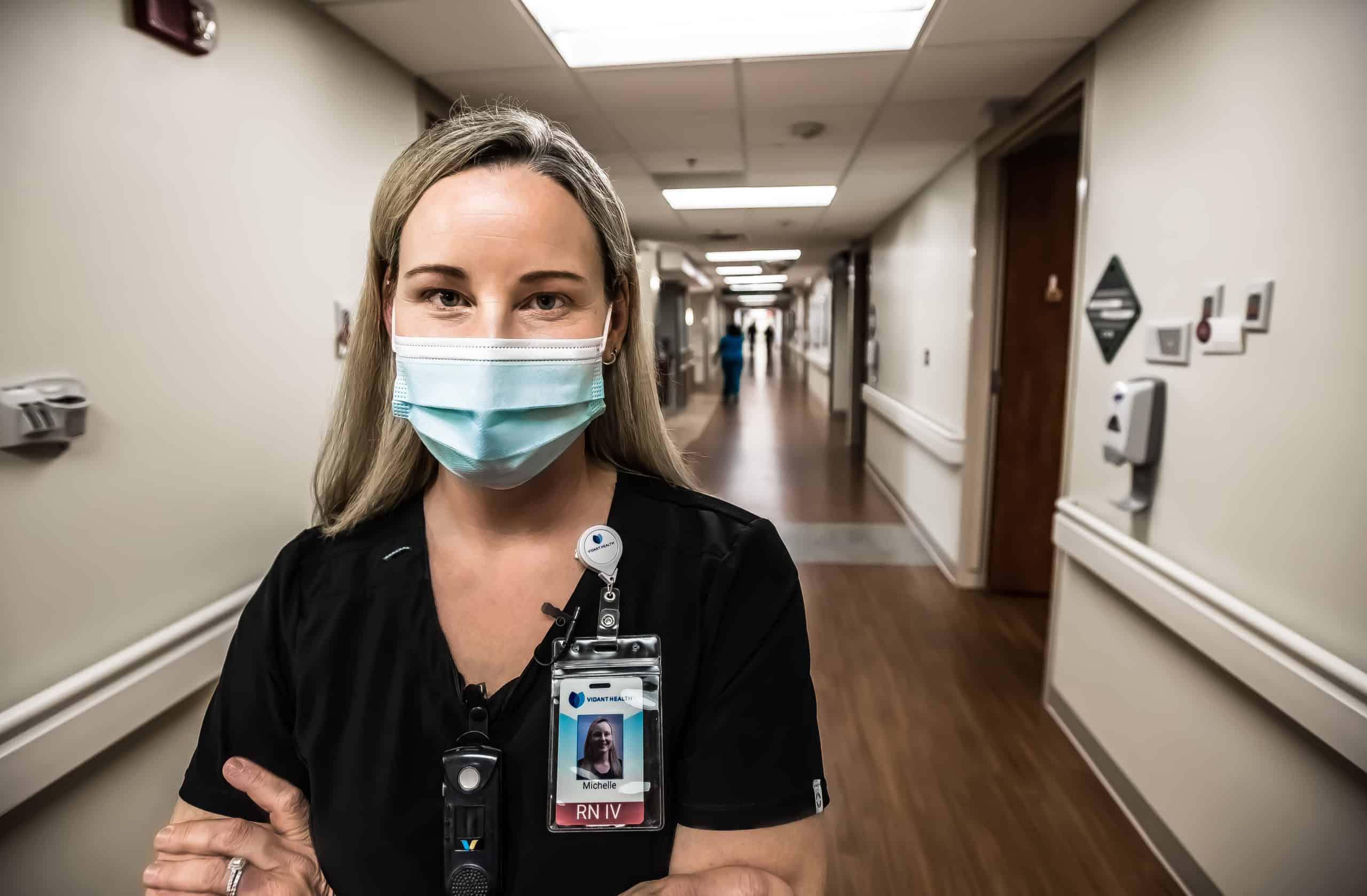 ECU Health nurse Michelle Kelley poses for a photo, wearing a mask with her arms crossed, in a hallway at ECU Health Medical Center.