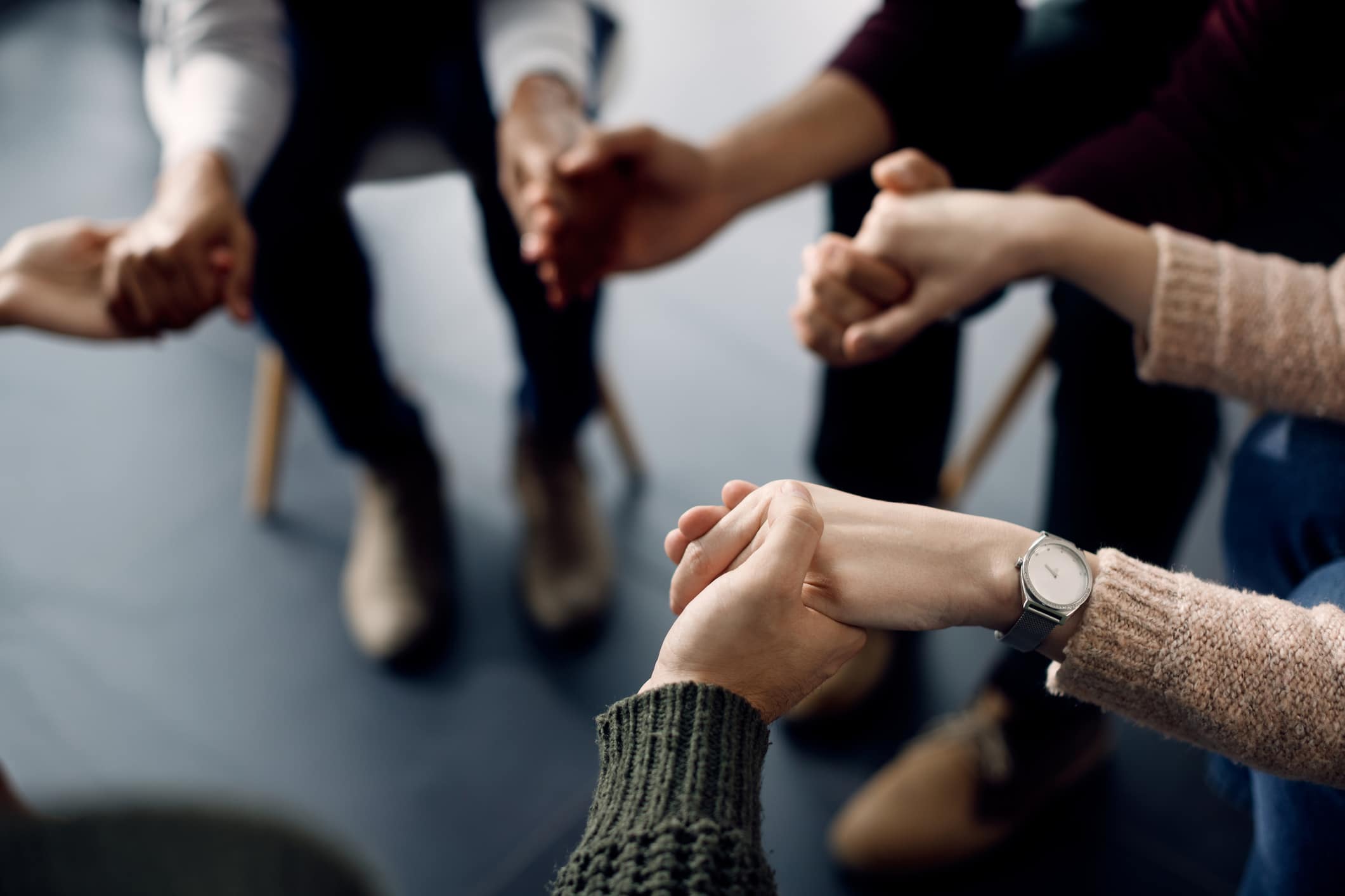 Close-up of people holding hands while sitting in a circle during a support group meeting.