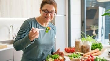 A woman eats a healthy vegan salad plate in her kitchen.