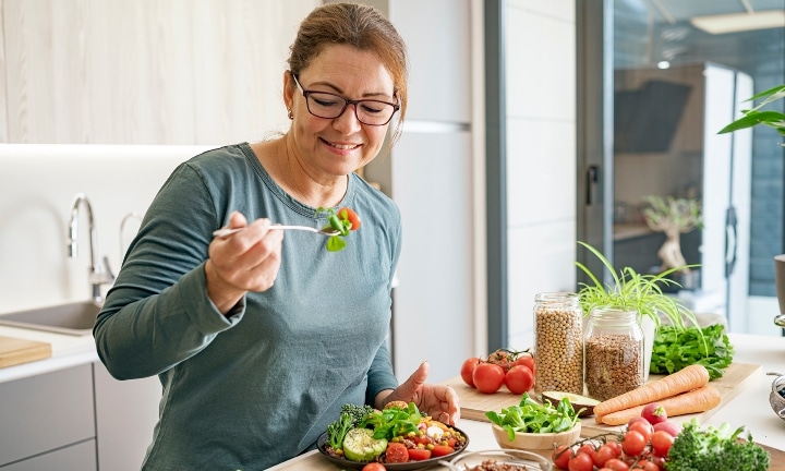 A woman eats a healthy vegan salad plate in her kitchen.