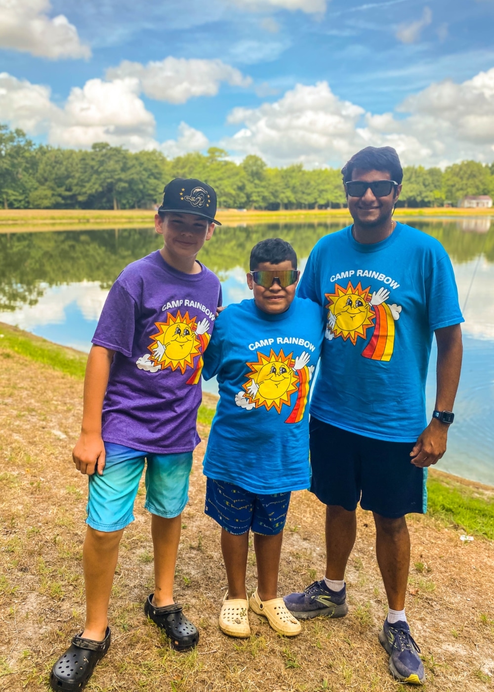 Two campers and a volunteer pose for a photo near the water at Camp Rainbow.