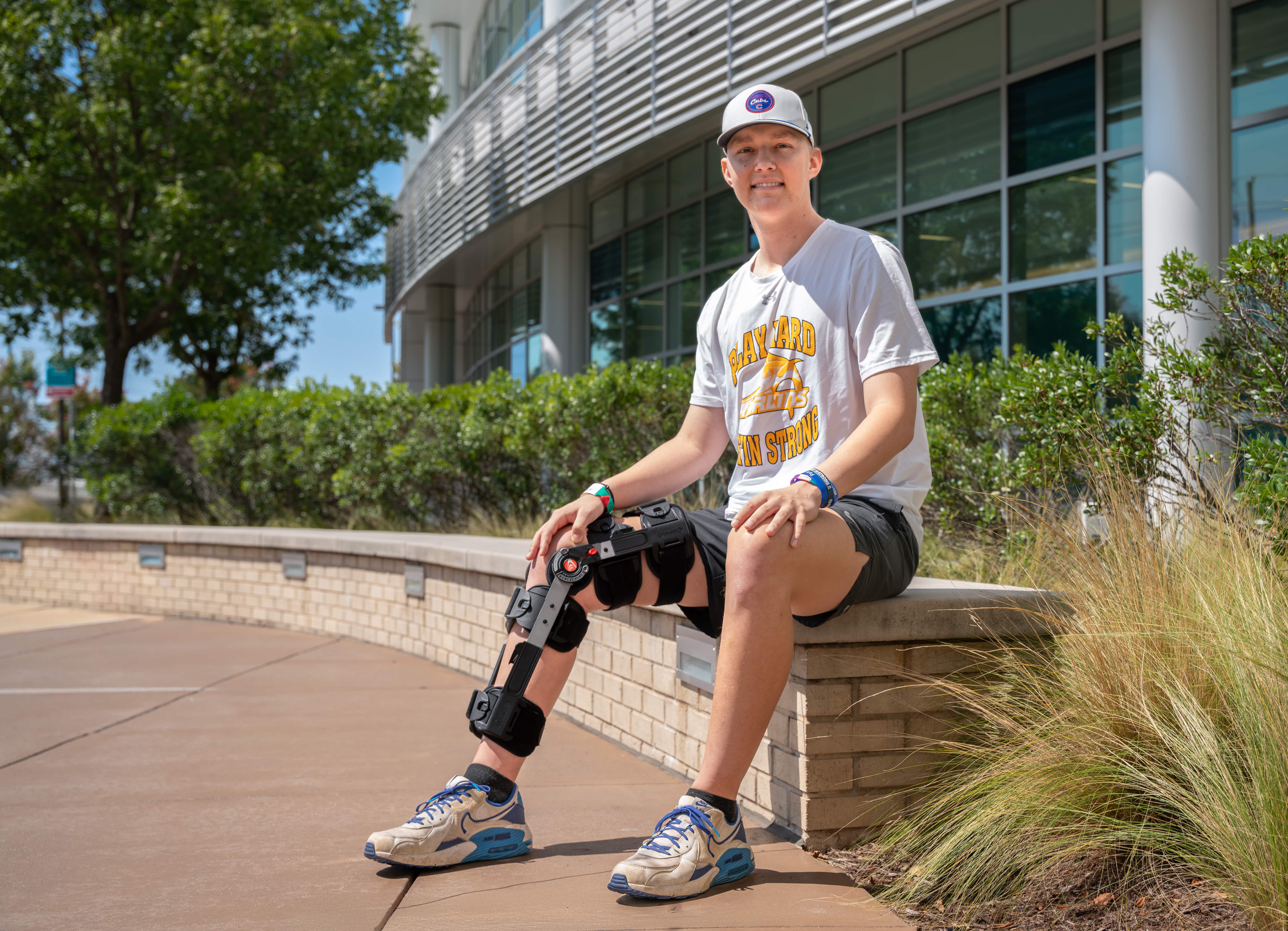 Austin Cherry, a patient at Maynard Children's Hospital, sits on a short wall outside of the Children's Hospital entrance.