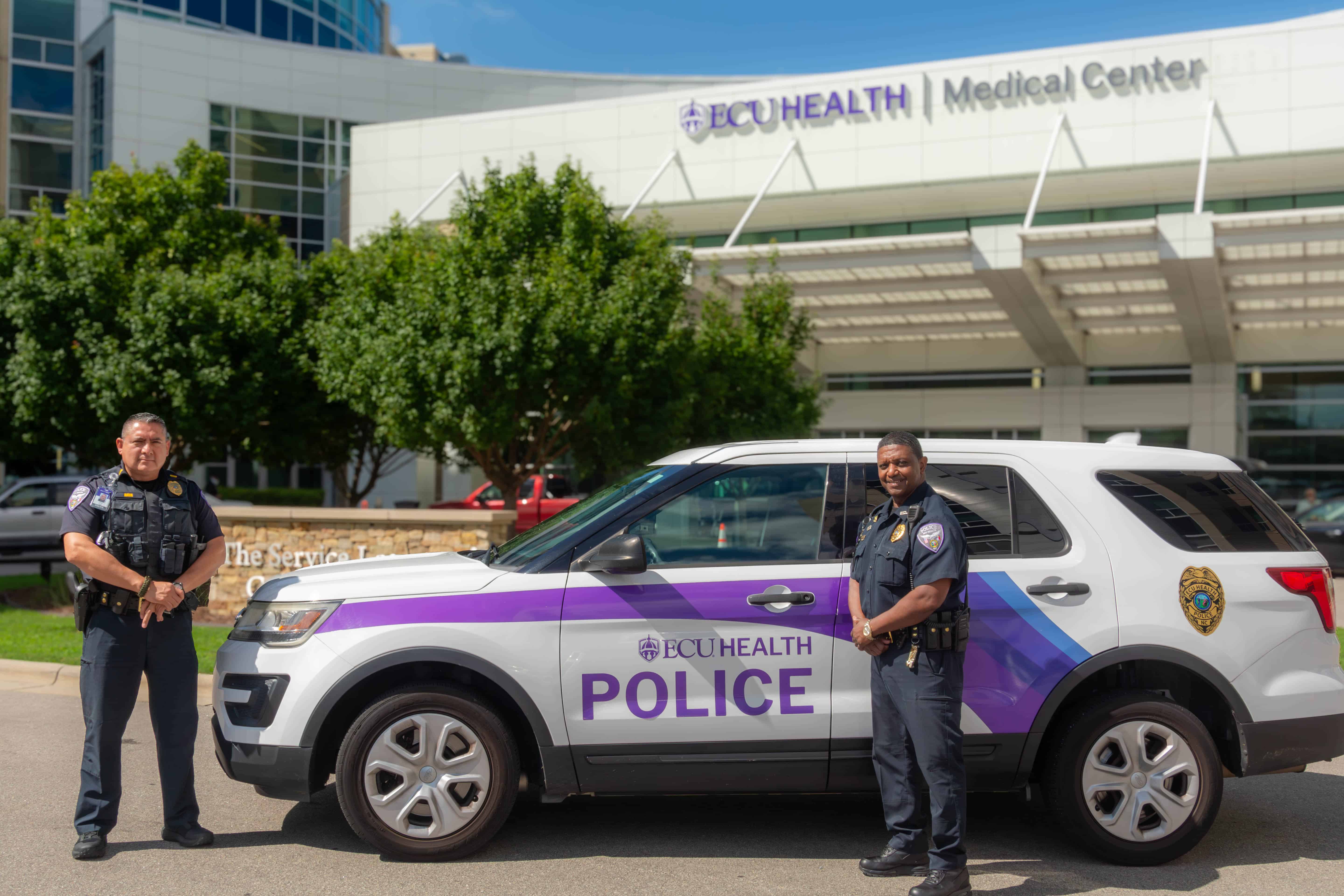 Two ECU Health Police officers stand by an ECU Health Police Department SUV in front of ECU Health Medical Center.