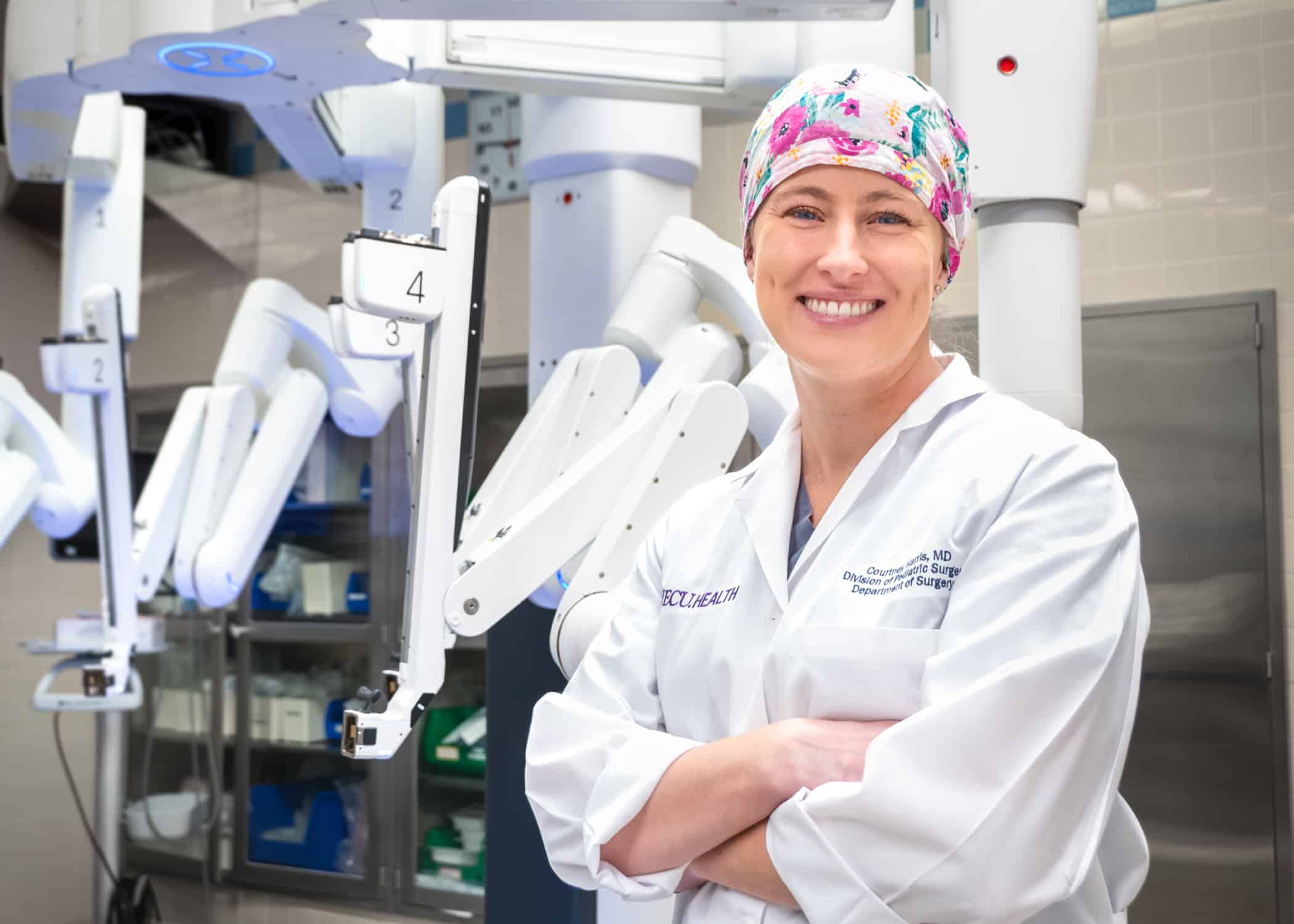 Dr. Courtney Harris, a pediatric surgeon at ECU Health, stands in front of Di Vinci robotic surgery equipment.